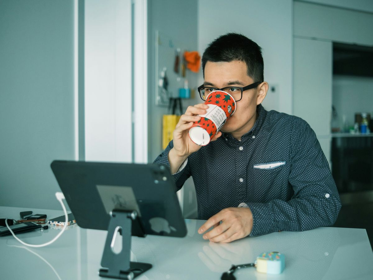 man in black and white checkered dress shirt drinking from brown and white ceramic mug