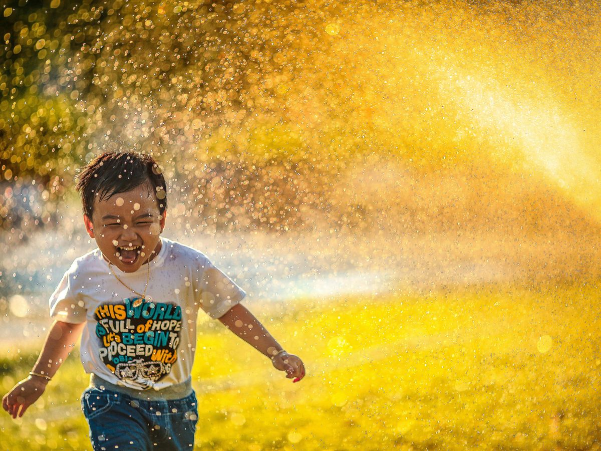 a young boy running through a sprinkle of water